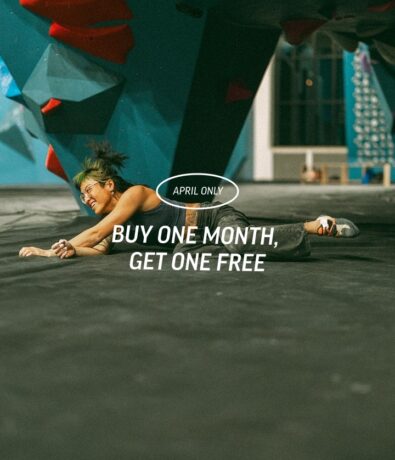 A person smiles while lying on a climbing gym floor with climbing walls in the background. Text reads: April Only. Buy One Month, Get One Free.