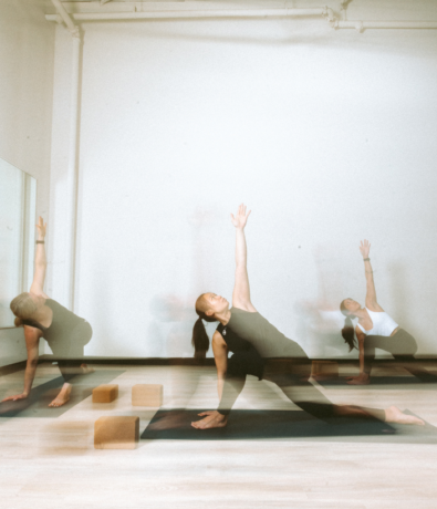 A yoga instructor and two students do a revolved low lunge pose in a yoga class