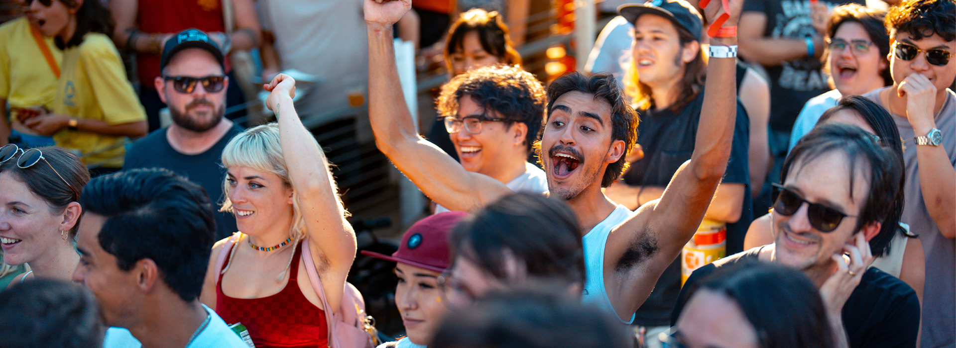 A diverse crowd of people outdoors at Boulderfest 2024 in Austin, smiling and cheering excitedly, with some raising their arms in celebration. The sunlight adds a warm, lively atmosphere to the scene.