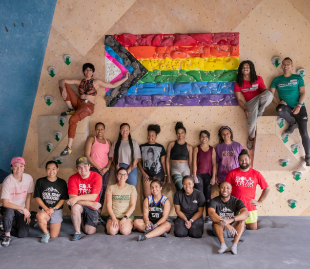 Stonewall Climbing group posing in front of a pride flag made out of climbing holds at bouldering project in dc.