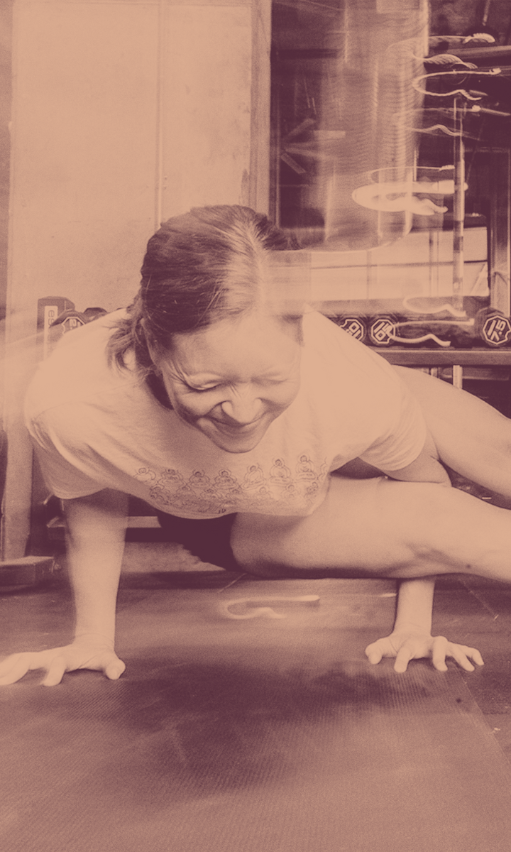 A woman balances on her hands in a yoga pose, smiling with effort. The sepia-toned photo, part of our Fall Promo 2025 for All Markets, features motion blur and fitness equipment in the background for a dynamic, energetic feel.