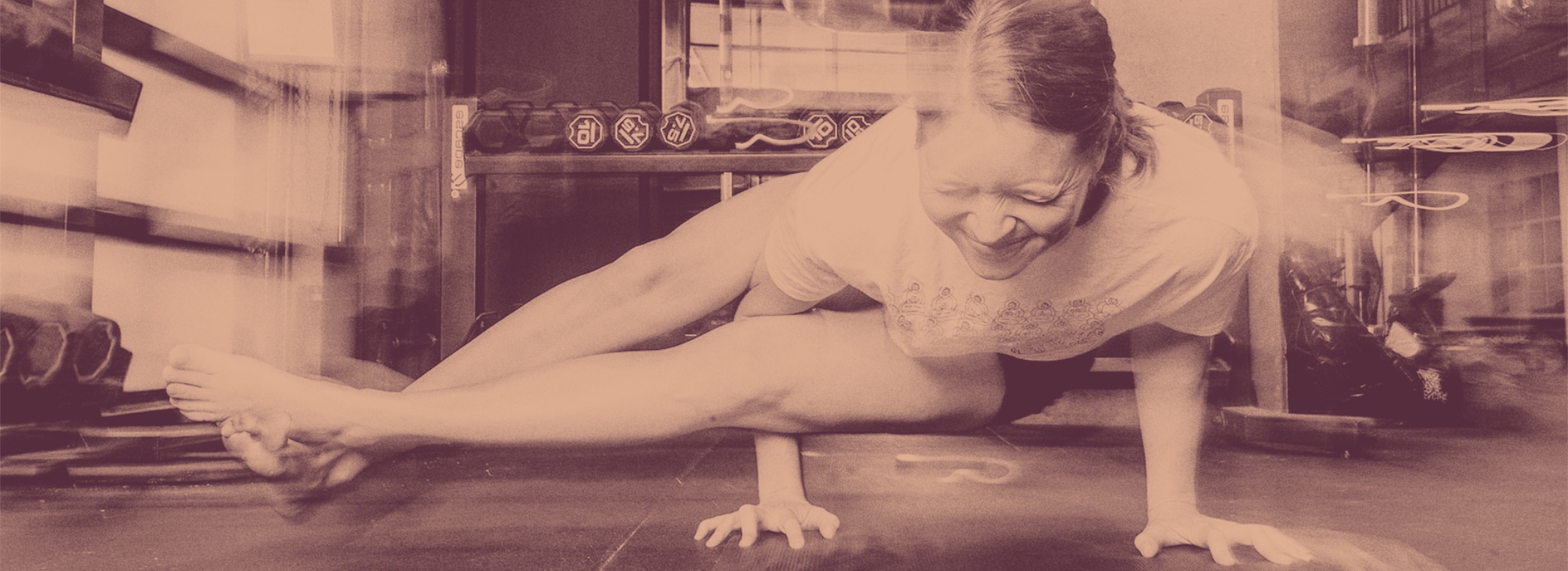 Woman balancing on one arm in a yoga pose indoors, smiling with eyes closed. The sepia-toned image, highlighting motion blur and effort, invites you to embrace movement—perfect inspiration for your fall membership journey.