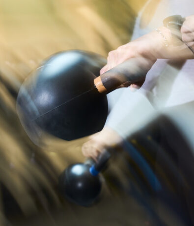 A person swings a black kettlebell, captured in motion blur—perfect inspiration for your Fitness Calendar. Their hand firmly grips the handle, and their forearm and wrist are visible, with a blurred background suggesting movement.