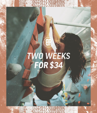 A woman climbs an indoor rock wall in Austin, smiling, with text overlay: Two Week Intro Pass for $34. The background features a warm-toned border and the logo above the offer.
