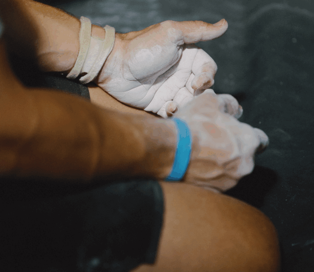 Close-up of a person's hands and arms with chalk dust, wearing wristbands, preparing for an athletic activity—possibly rock climbing or gymnastics—with a focus on BP Personal Coaching, set against a dark background.