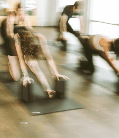 A blurred image of people in a yoga class, stretching forward on yoga mats and using yoga blocks for support in a bright indoor studio—perfect inspiration for your fall membership.