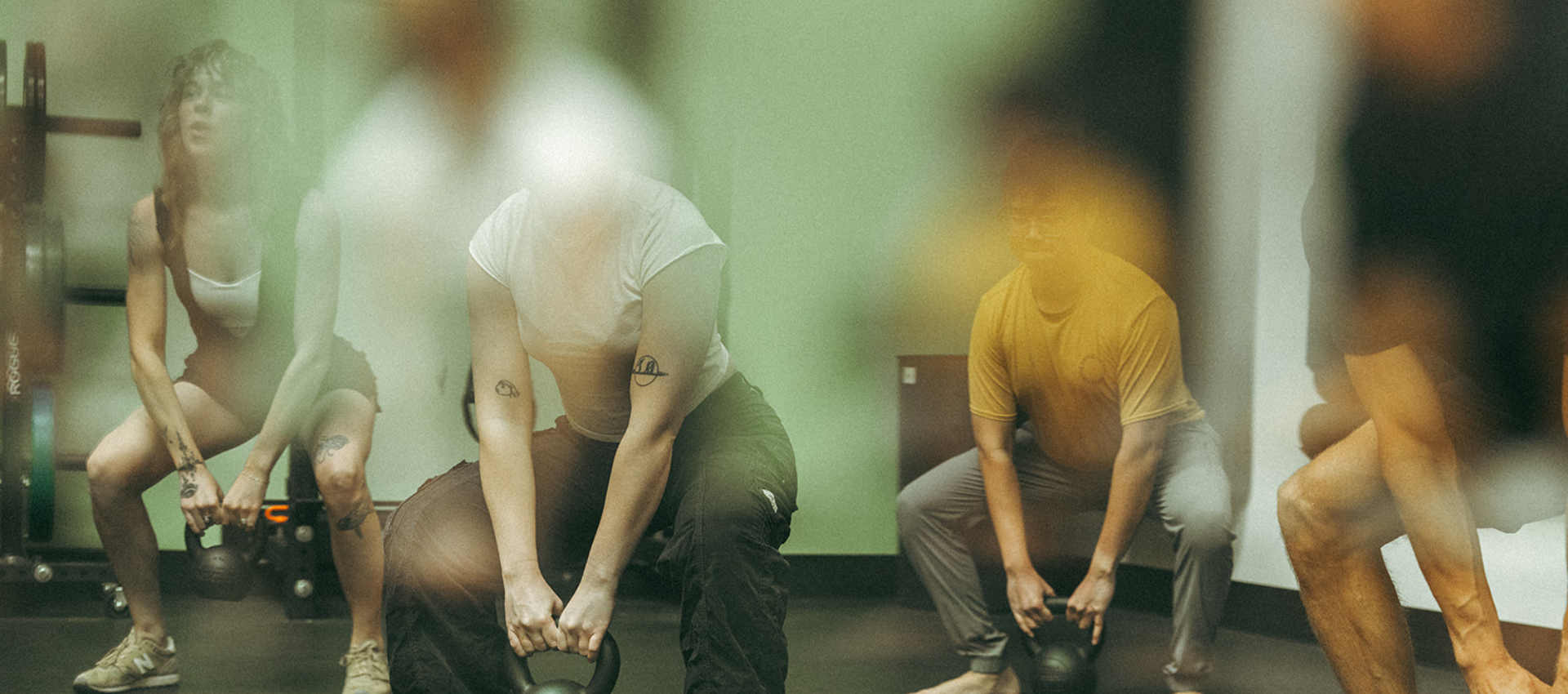 Several people are exercising indoors, bending down while holding kettlebells. The image is slightly blurred and features reflections or light spots, adding a soft, hazy effect—perfect inspiration to train smarter with focused climbing exercises.