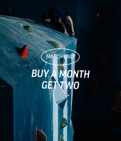 A person climbs an indoor bouldering wall with colorful holds. Text overlay reads: March Only. Buy a month, get two membership deals. The setting is dimly lit with blue tones at Springdale's best pricing.