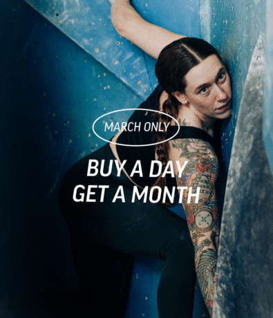 A woman with tattoos climbs an indoor rock wall at Springdale, looking up. Overlaid text reads: March Only. Buy a day, get a month—special membership pricing!.