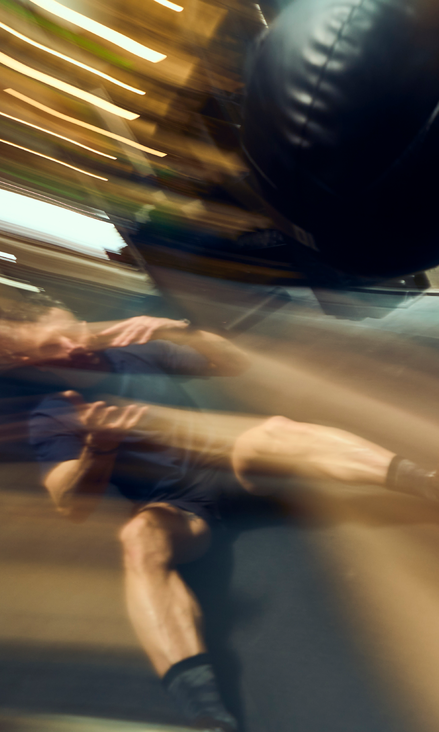 A person in motion, blurred as they sit on the floor of an Austin gym, with a punching bag swinging nearby, capturing the dynamic energy of a fitness challenge.