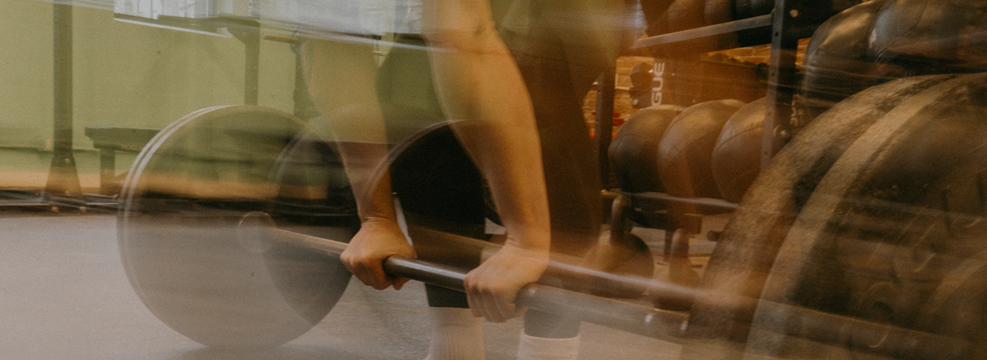 A person with blurred motion prepares to lift a barbell in a gym, surrounded by weights and exercise equipment, enjoying Membership Benefits at Seattle Bouldering Project.