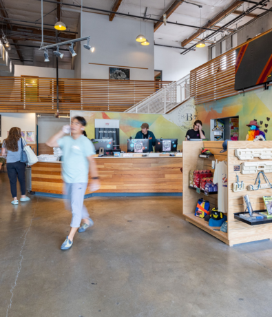 A modern indoor space with people near a wooden counter, shelves with products, and a staircase leading to an upper level—showcasing Membership Benefits at Seattle Bouldering Project as members gather and connect.