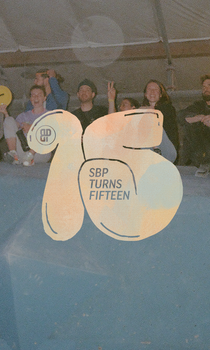 A group of people sit and smile behind a blue barrier at a Seattle climbing competition, with large, stylized orange numbers 15 and the text SBP TURNS FIFTEEN overlaid on the image.