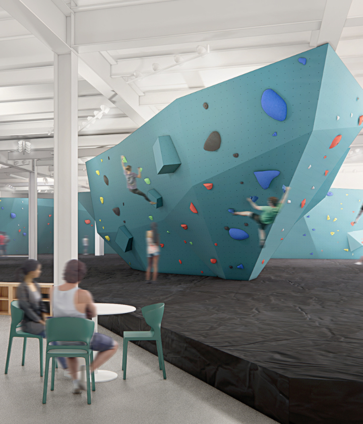 A modern dc climbing gym with people bouldering on a large, angular blue climbing wall. Two people sit at a table in the foreground, while others climb on colorful holds in the background.