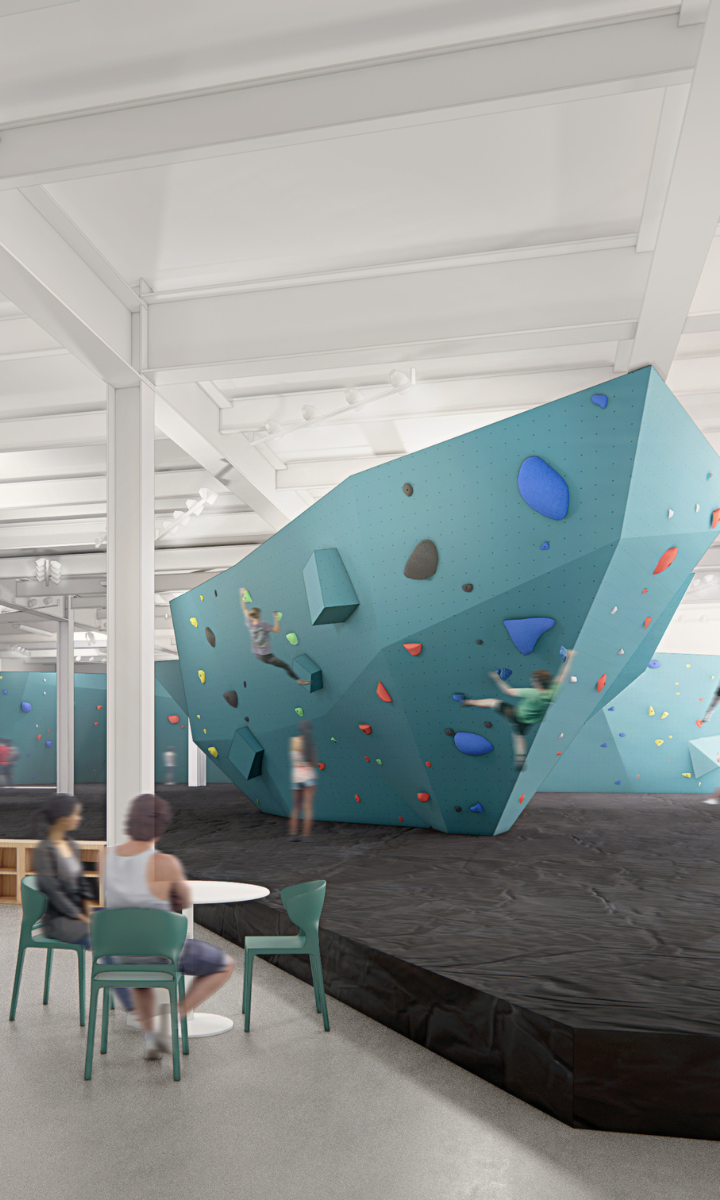 A modern dc climbing gym with people bouldering on a large, angular blue climbing wall. Two people sit at a table in the foreground, while others climb on colorful holds in the background.