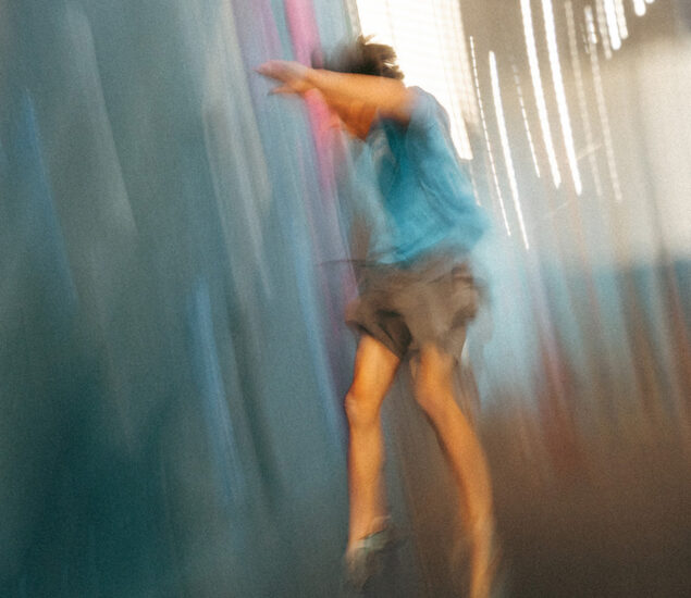 A blurred image of a person in mid-air, wearing a blue shirt and shorts, against a colorful background, evokes the energy and excitement of a Seattle climbing competition.