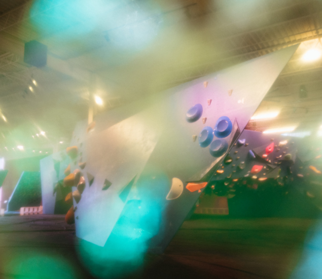 Blurred image of an indoor climbing gym with geometric climbing walls, colorful holds, and soft lighting. Hazy green and blue areas obscure parts of the scene, creating a dreamy effect—perfect for showcasing upcoming climbing classes.