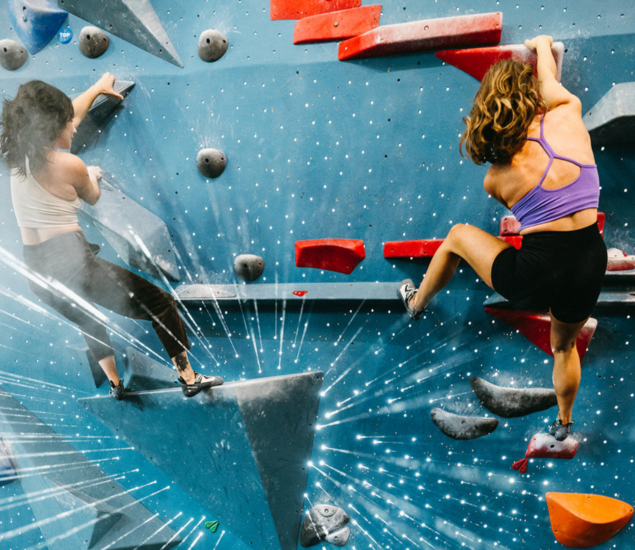 Two women are climbing a blue indoor bouldering wall with red and gray holds, showcasing skills learned in climbing classes. Both wear athletic clothing and climbing shoes, while bright white lines add a dynamic effect to the scene.