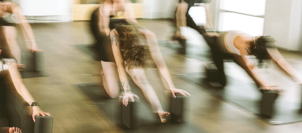 A group of people practicing yoga indoors, all in a stretching pose using yoga blocks, with motion blur creating a dynamic effect—much like exploring how to choose the right climbing gym for your fitness journey.