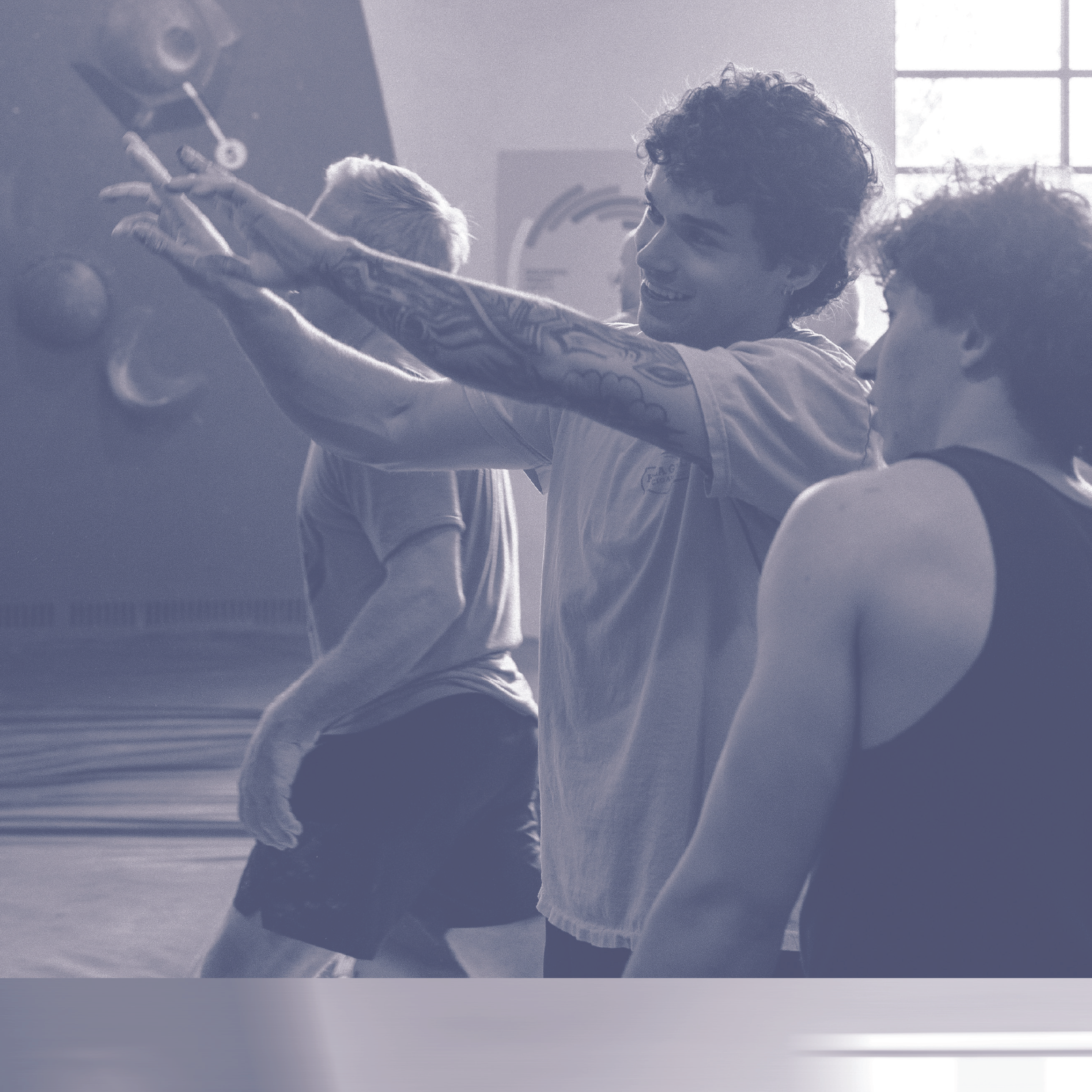 Three people in athletic wear are in a gym. One person with tattoos is pointing excitedly while the others watch. The background includes climbing walls and a large window letting in sunlight, capturing the energetic spirit of Austin’s 2025 Fall Promo.