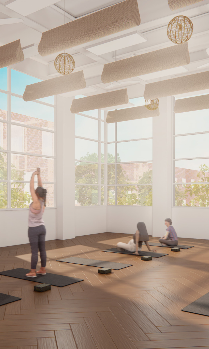 A bright yoga studio with large windows; one person stands stretching on a mat while three others sit or lie on mats. Sunlight streams in, highlighting the wooden floor and modern hanging lights, creating a serene escape just steps away from the bustling energy of the nearby dc climbing gym.
