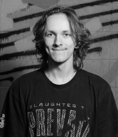 A black and white portrait of a young person with long hair, wearing a black t-shirt with stylized graphic text for a Bouldering Project climbing competition.