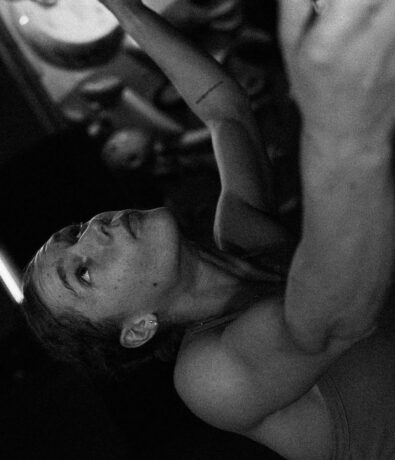 A person reaches for a hold during a bouldering project, looking up toward their hand as they climb.