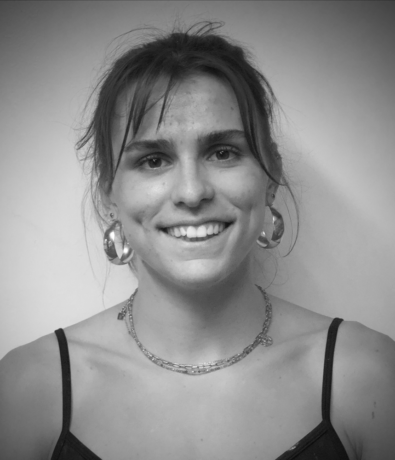A young woman smiling at the camera, wearing large hoop earrings and a layered chain necklace while attending the Bouldering Project community climbing competition.