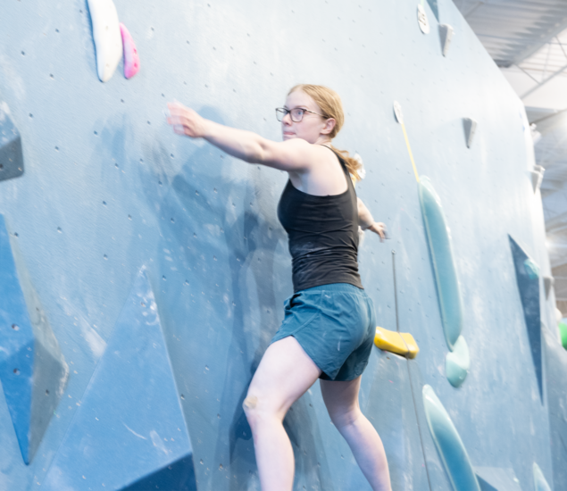 A climber reaching for a hold on an indoor bouldering wall at an Austin climbing gym.