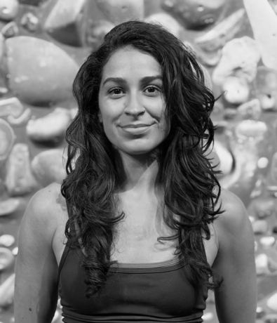 A woman stands in front of a climbing wall with handholds during a bouldering project.