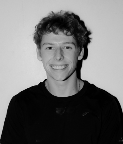 A young man with curly hair smiles at the camera during the Boulderfest climbing competition.