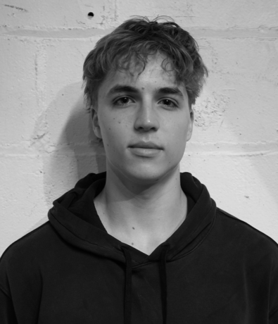 A young man in a hoodie poses against a white brick wall during a Bouldering Project climbing competition.