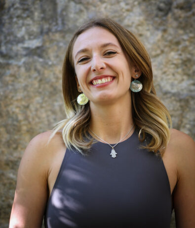 A smiling Salt Lake City personal development coach wearing circular patterned earrings and a hamsa hand necklace.