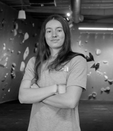A young woman with her arms crossed stands in a bouldering gym during a local boulderfest.