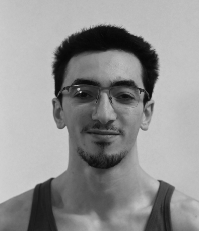 A black and white portrait of a young man with short hair, a goatee, and glasses at the Boulderfest bouldering project.