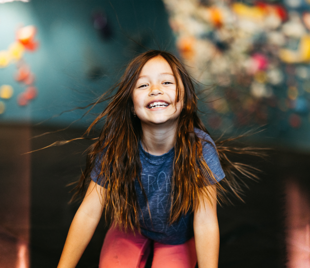 A young girl with long hair windswept around her face smiles broadly, capturing the spirit of Austin youth programs.