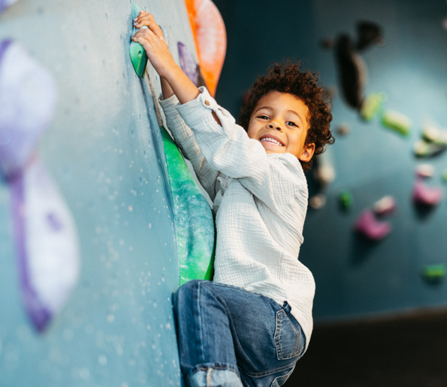 A smiling child climbing a rock wall at a Tempe youth climbing club.