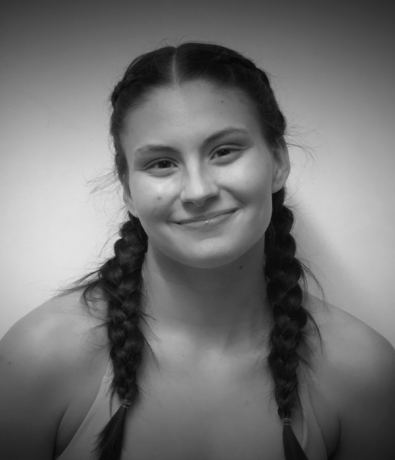 A young woman with two braids smiles at the camera during a Bouldering Project climbing competition.