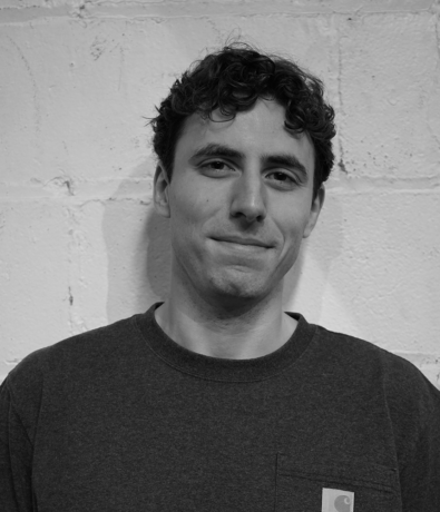 A black and white portrait of a man with curly hair wearing a crewneck sweatshirt at a Boulderfest community climbing competition.