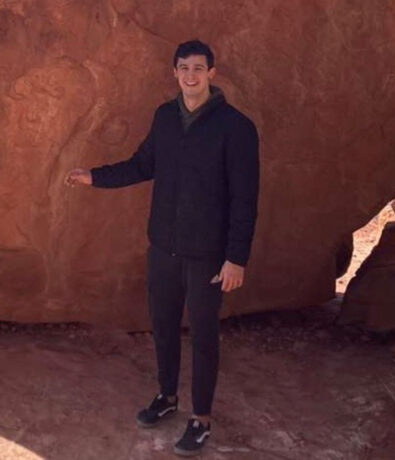 A man in a black jacket and sweatpants standing in front of a large red rock formation, representing a Tempe personal coaching session.