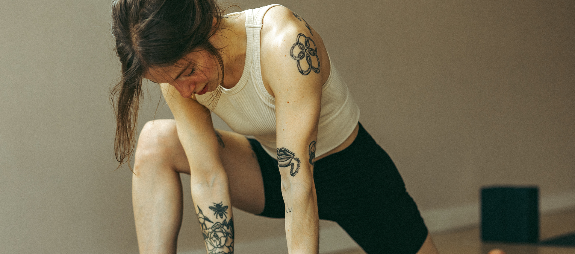 A person with tattoos on their arms and shoulder performs a lunge in a mat Pilates studio.